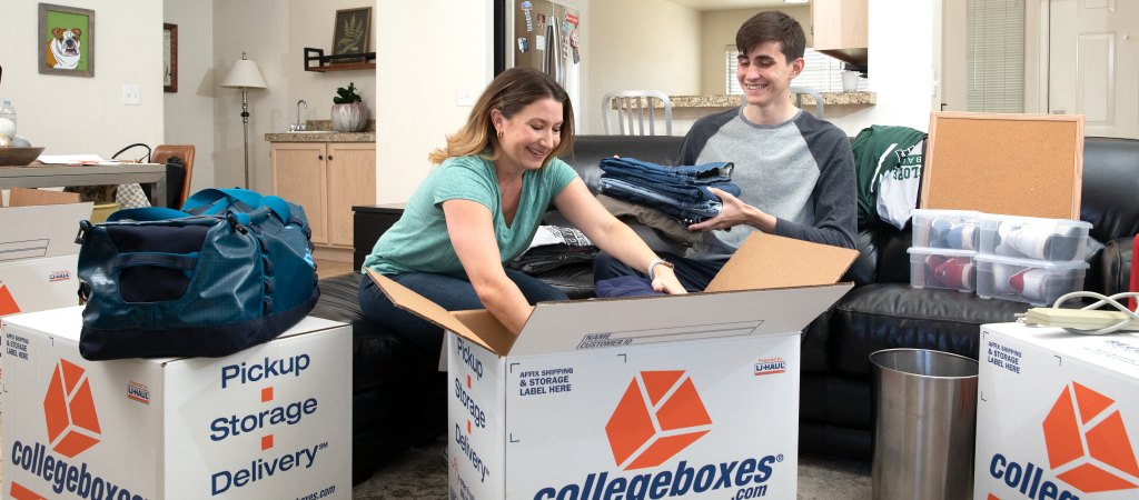A mother and son pack clothes in a box for college.
