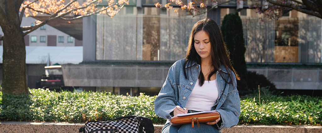 College student sitting on a bench and writing