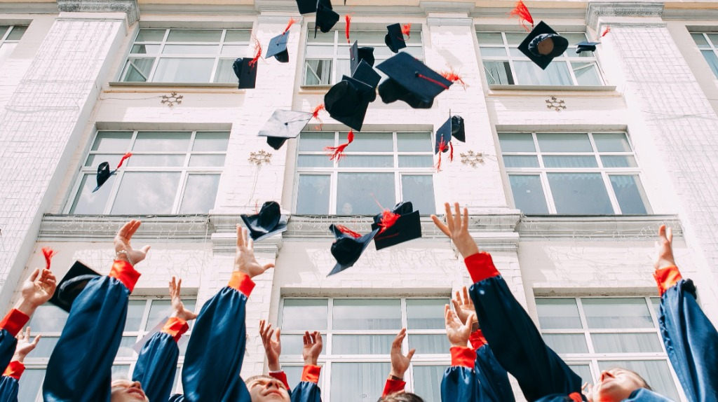 College graduates celebrating by tossing their caps in front of an academic building.