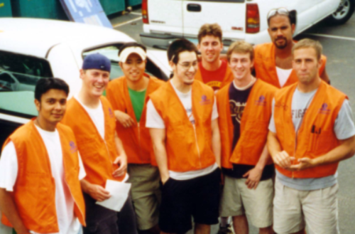 Group of college boys in orange vests stranding in front of a pickup truck.