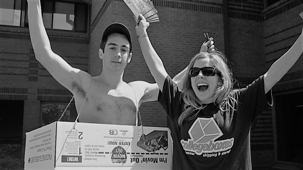 Girl with sunglasses stands next to a shirtless man that is wearing a box over his torso. Both are cheering.