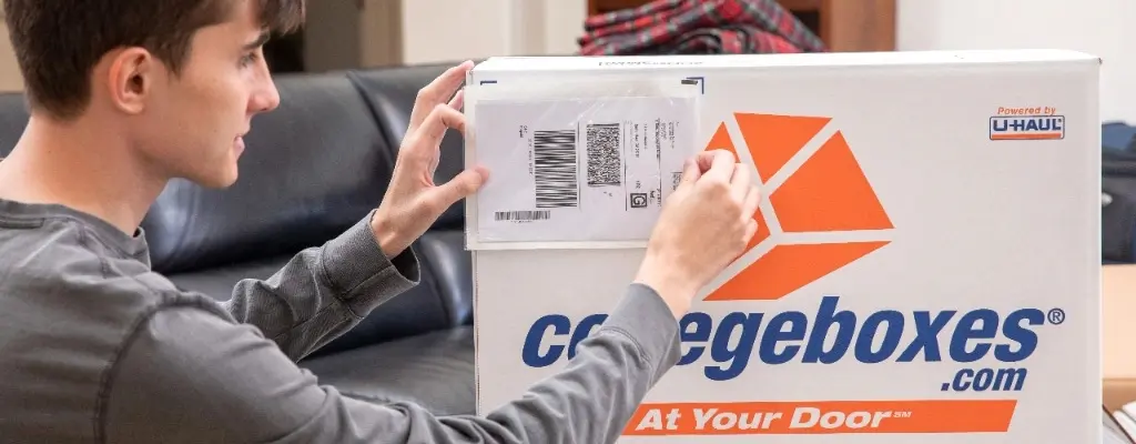 oung brunette man placing a shipping label on a Collegeboxes box.