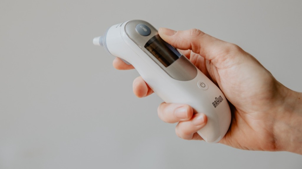 Woman's hand holding a digital thermometer over a gray background.