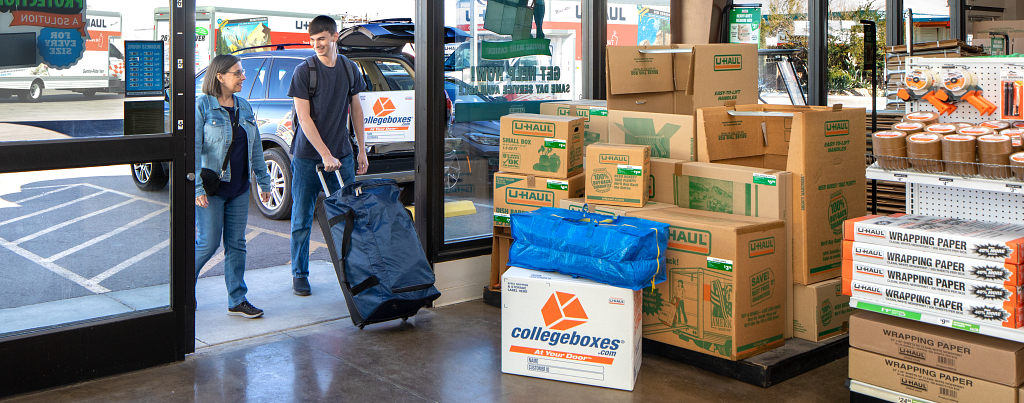 A young man with luggage walks into a U-Haul with an older woman.