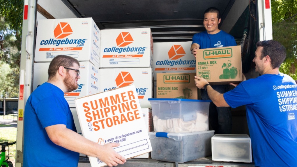 One man stands inside a full moving truck, handing a box to the two men standing outside.