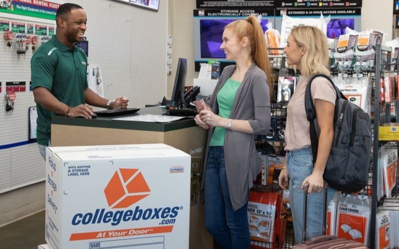 Two young women stand at a counter with a U-Haul worker.