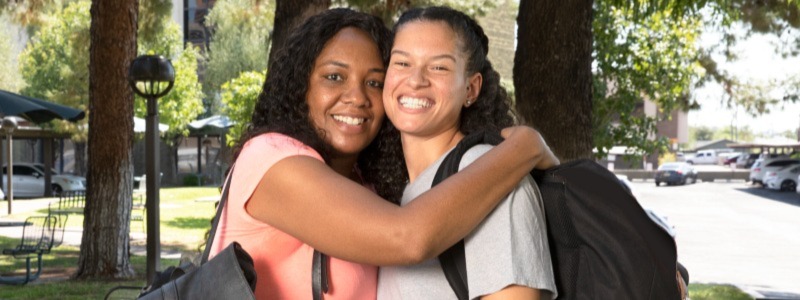An older woman embraces a young woman with a backpack on.