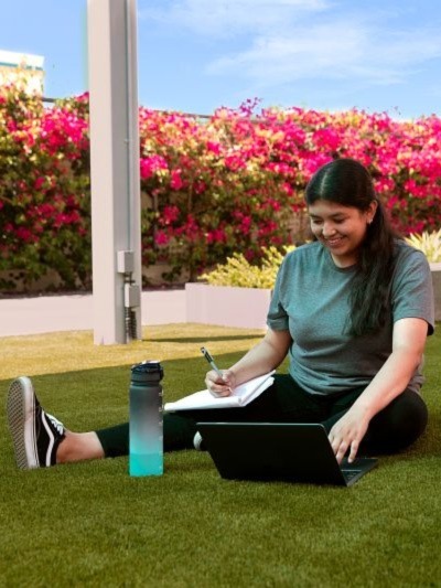 Girl sitting on grass and writing in a notebook.