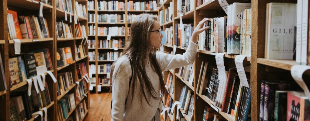 A girl with long hair and glasses looking at books in a library