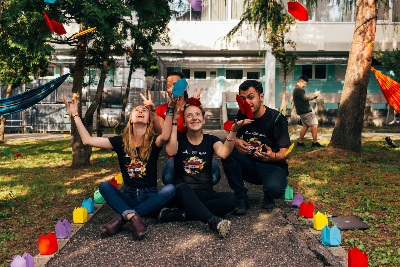 Three college students in club shirts sitting on the ground and tossing papers