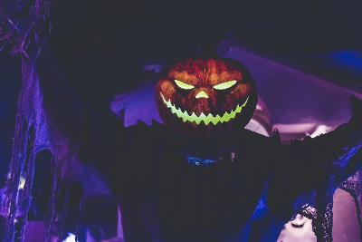 Man in dark room wearing a pumpkin head with glowing eyes.