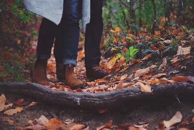 Two women's legs and shoes walking through leaves.