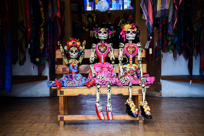 Three colorful skeletons sitting on a tiny bench.