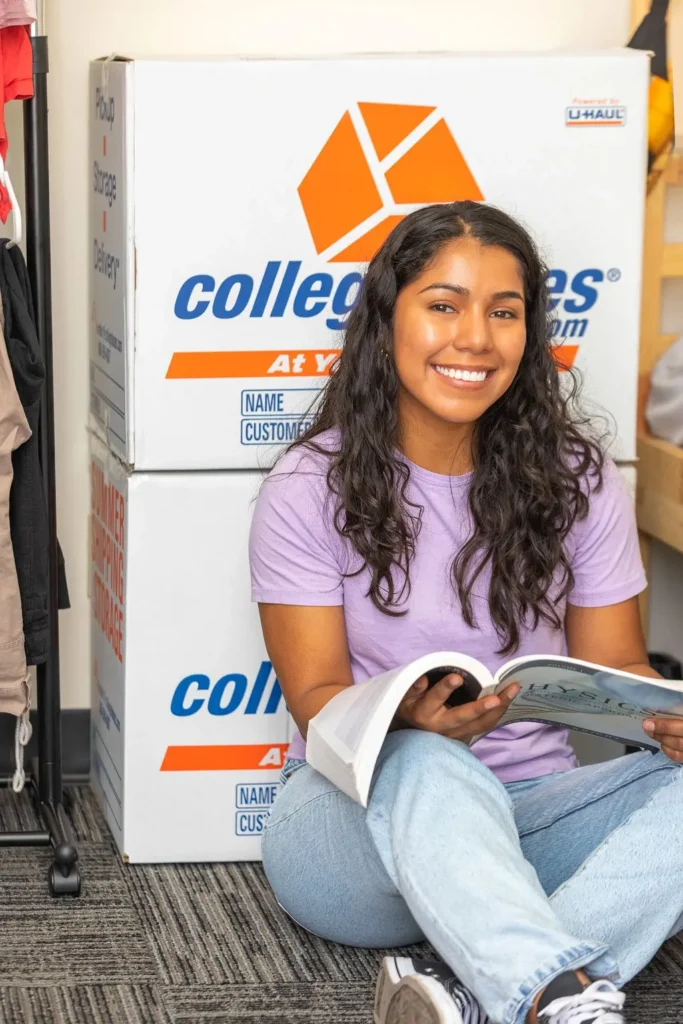 Girl sitting on the ground, reading a book in front of Collegeboxes 