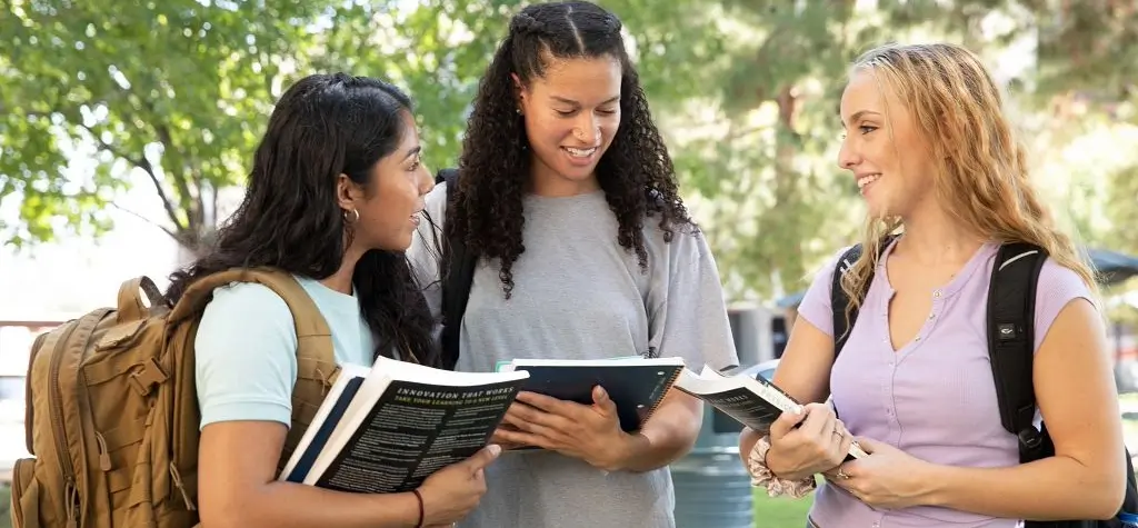 Three girls holding books and talking to each other