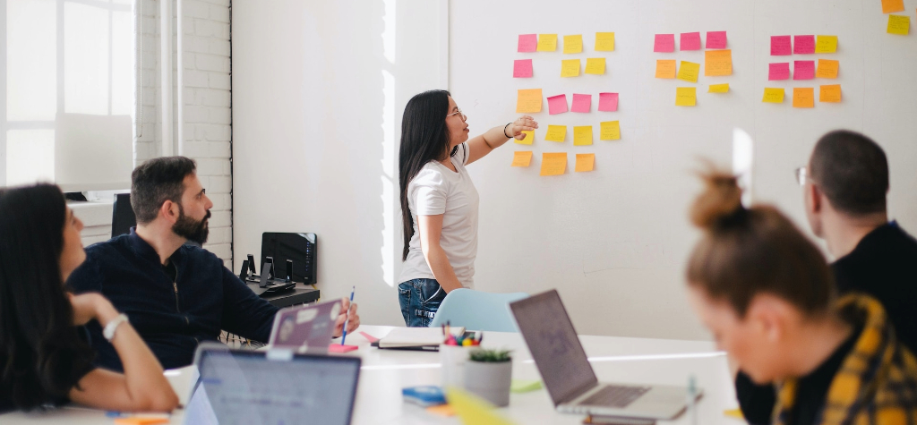 Girl standing in front of a whiteboard covered in sticky notes.
