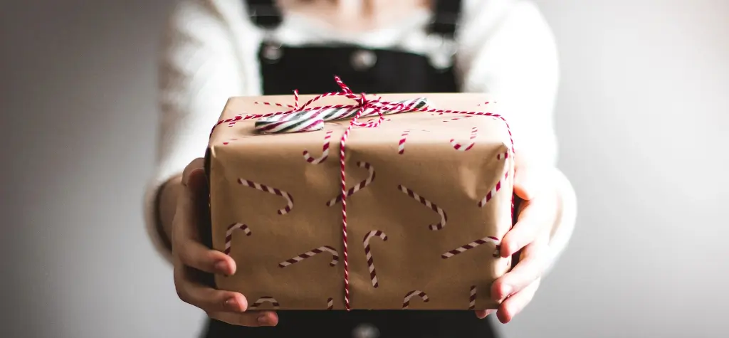 Girl holding a gift wrapped in brown paper with candy canes.