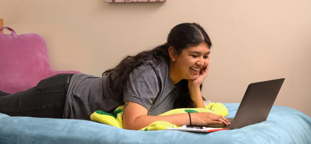 A college student in her dorm looking at a laptop.