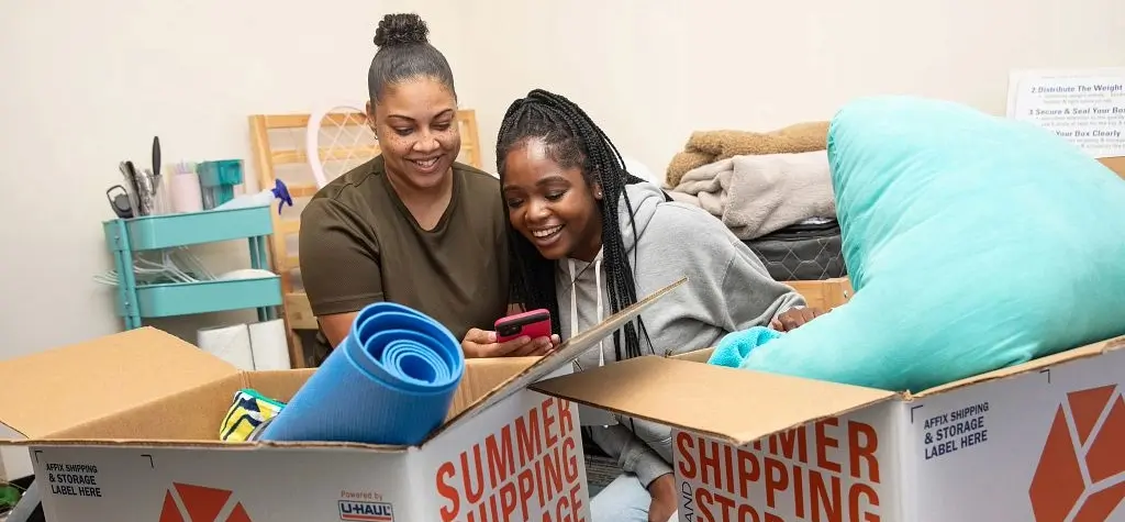 Two women sitting on the ground among boxes and looking at a phone