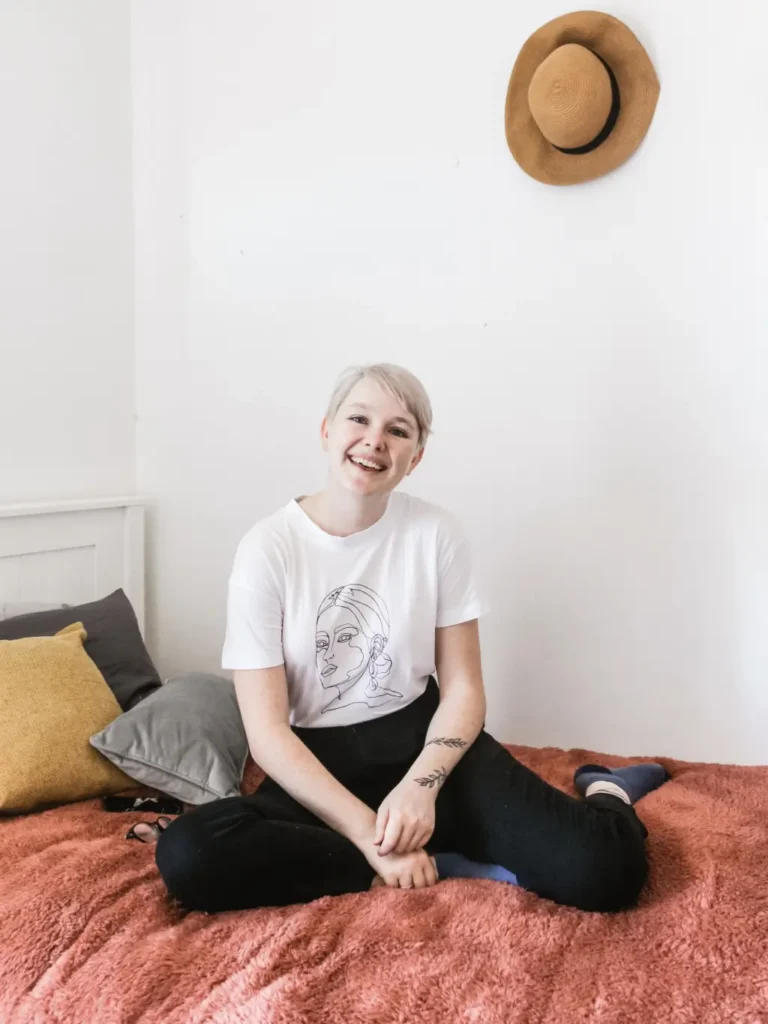 Girl in white shirt and pants smiling on her bed 