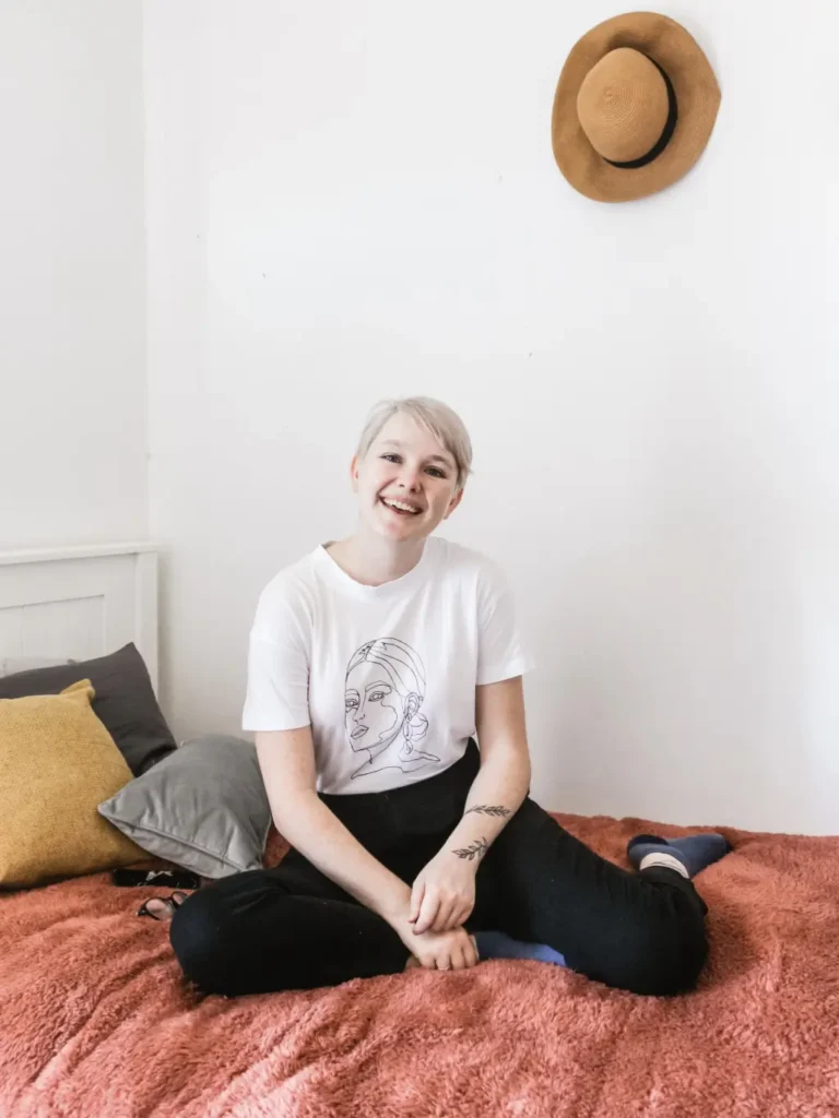 Girl in white shirt and pants smiling on her bed