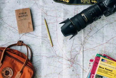 A camera, notebook, bag, and book ontop a map