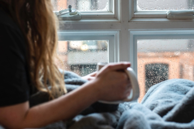 Girl under a blanket with a mug looking out the window
