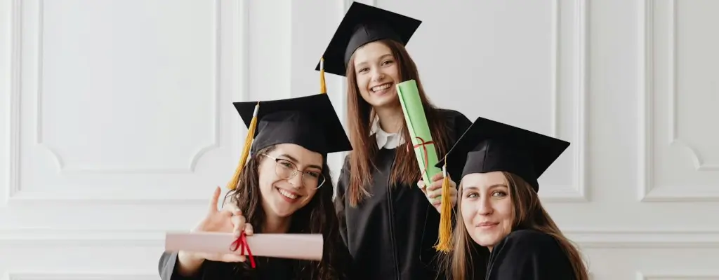 Three girls in graduation gowns, caps, and holding their diplomas