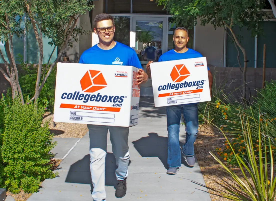 Two movers each holding CollegeBoxes branded boxes walking towards the camera