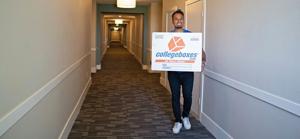 Man walking down an empty hallway with a box