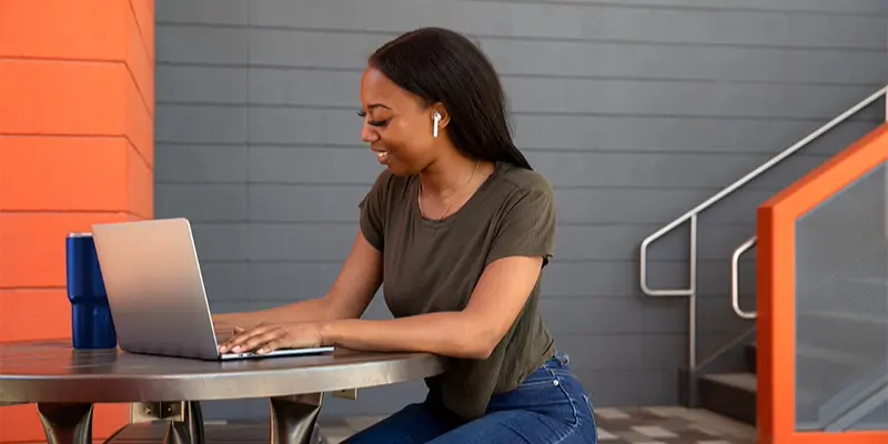 Girl sitting at an outdoor table, typng on her laptop