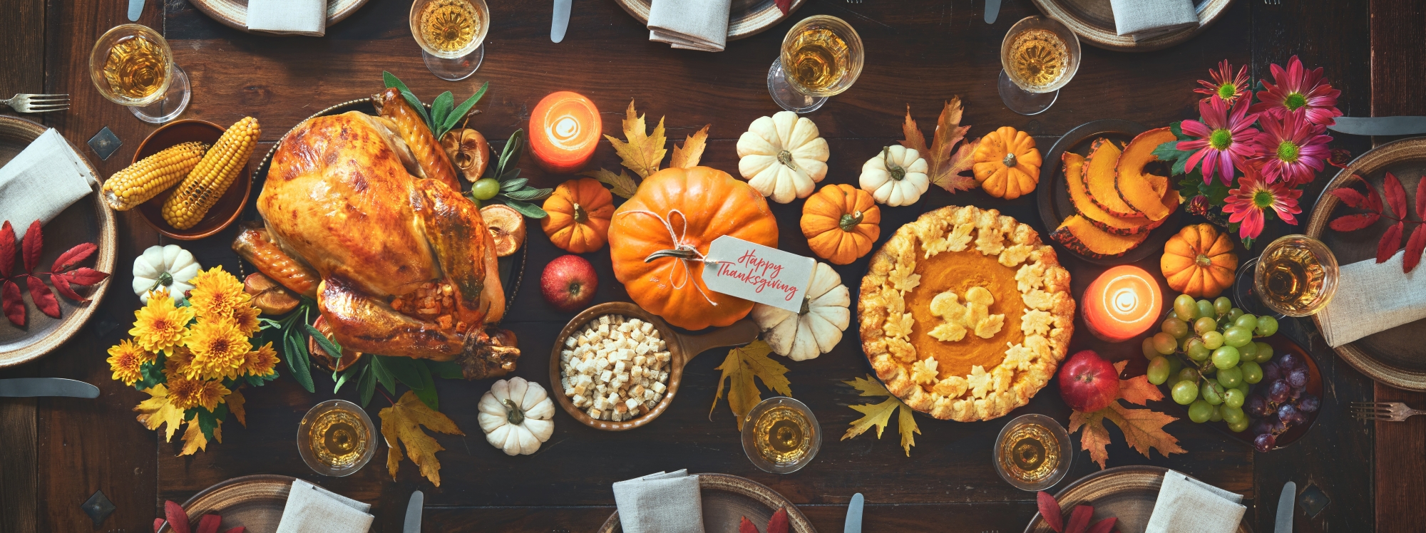 Festive Thanksgiving table with roasted turkey, pumpkin pie, corn, grapes, decorative pumpkins, candles, and flowers, evoking warmth and gratitude.